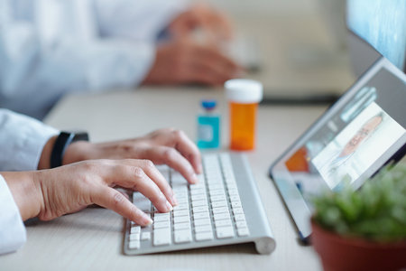 Hands of chief physician working on computer when having online meeting with colleague from another...