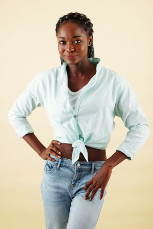 Portrait of confident smiling young woman in jeans and mint shirt standing with hands on hips and...