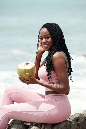 Portrait of beautiful young woman in sportswear drinking coconut cocktail and smiling at cameraの写真素材