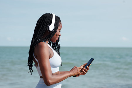 Smiling fit young woman in headphones choosing music for her traning via application on smartphone