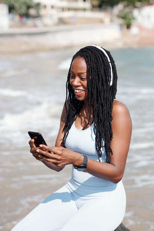 Joyful young woman sitting on beach and video calling her coach or friendの写真素材