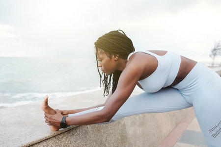 Flexible fit young sportswoman streching legs on embankment after jogging in the morning