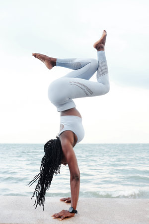 Fit strong young sportswoman doing handstand on embarkment with beautiful sea in background