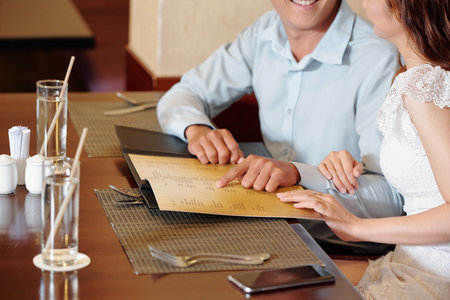 Cropped image of smiling young couple pointing at restaurant menu and discussing what beverage and...