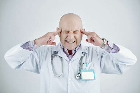 Annoyed mature Caucasian doctor with bald head closing eyes and touching temples while suffering from headache, isolated backgroundの写真素材