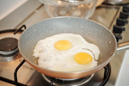 Close-up of cooking pan with two fried eggs cooking on stove in kitchen