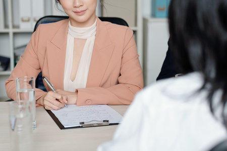 Smiling female human resources manager taking notes in document when talking to applicant at job interviewの写真素材