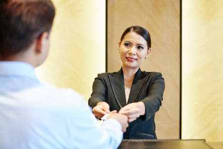 Smiling receptionist giving electronic key card to hotel guest with two handsの写真素材