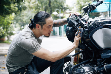 Handsome man cleaning and wiping his bike with soft cloth, motorcycle detailing or valeting concept