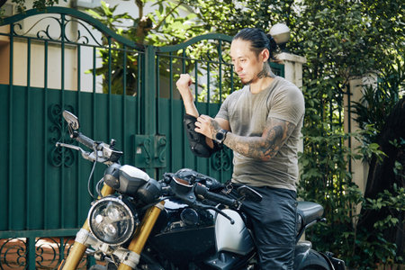 Serious motorcyclist sitting on bike and putting on forearm guard pads for protectionの写真素材