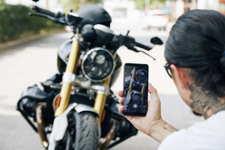 Man taking cool photos of his motorcycle on smartphone to share with friends or post on social mediaの写真素材