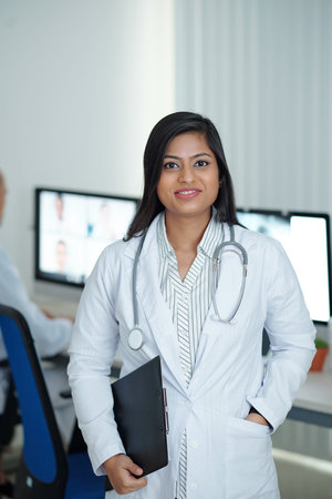 Positive young female physician standing in medical office with clipboard in hand ready to visit sick patientsの写真素材