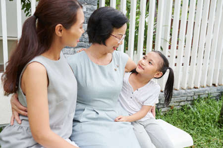 Smiling elderly woman hugging her daughter and granddaughter vising her for holidaysの写真素材