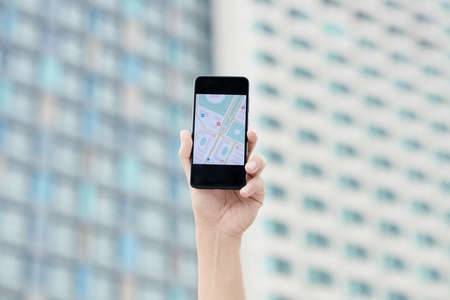 Close-up of male hand holding smartphone with online map on screen against city buildingの写真素材