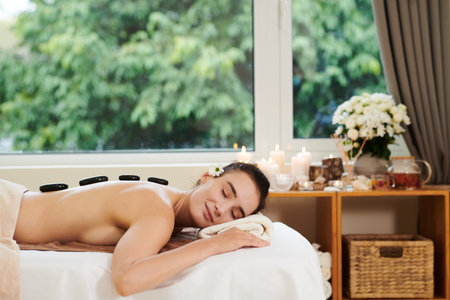 Young beautiful woman lying on the sofa with hot stones on her back and relaxing