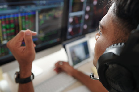 Close-up image of trader in headphones alayzing stock market data on screens in front of him