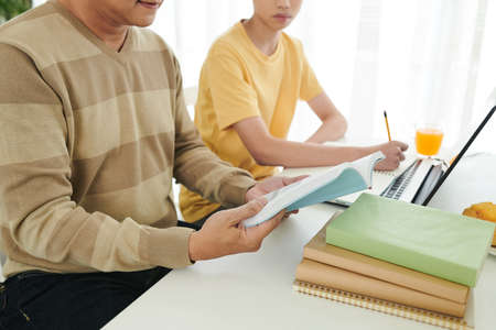 Father reading students book and explaining difficult topic to his teenage sonの写真素材