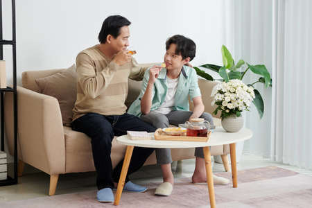 Teenage boy eating potato chips and discussing news with dad who is drinking teaの写真素材