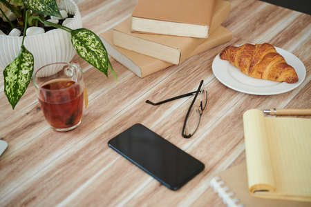 Stack of books, smartphone, tea and croissant on table of college studentの写真素材