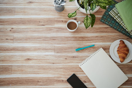 Table with notepad, books, croissant and cup of coffee, view from the top