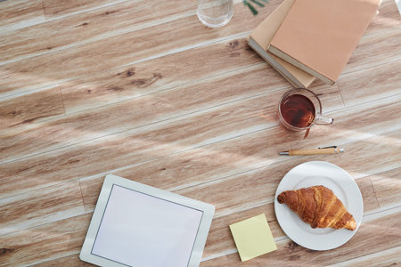 Digital tablet with empty screen, tea with pastry and stack of books on table of creative college student, view from aboveの写真素材