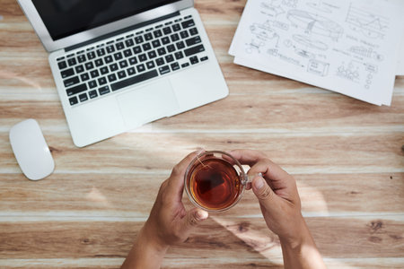 Hands of businessman drinking cup of tea to relax after finishing work on report or project