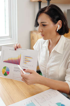 Female entrepreneur showing printed report with ascending column chart when talking to colleague at online meetingの写真素材