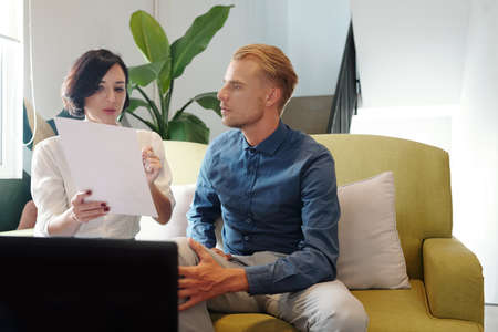 Young female entrepreneur pointing at chart in report when sharing her thoughts and conclusions with colleague at meetingの写真素材