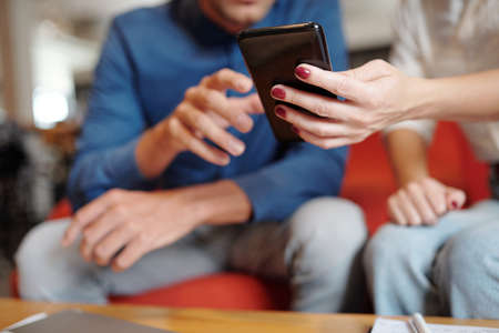 Close-up image of businesswoman showing message on smartphone to her colleague at meetingの写真素材