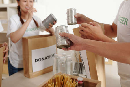 Male and female volunteers packing canned food and drinks in cardboard boxes for homeless peopleの写真素材