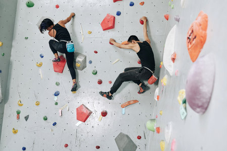 Fit strong young couple climbing up together on buildering wall when training for competition