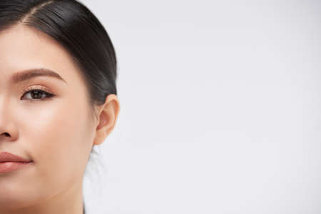 Half face of beautiful young woman looking at camera, isolated on whiteの写真素材
