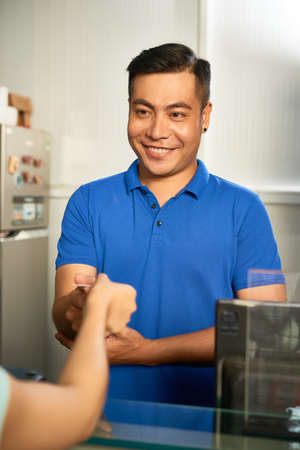 Handsome smiling cashier worker accepting payment with credit cardの写真素材