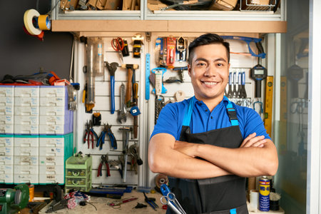 Portrait of happy confident mechanic in apron standing at workbench with various tools hanging...