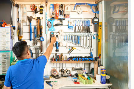 Mechanic taking tool from wall behind his workbench, view from te backの写真素材