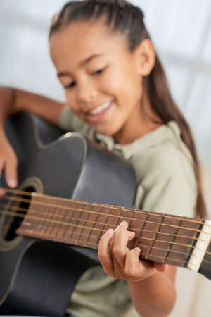 Smiling little girl learning to play guitar during lesson at homeの写真素材