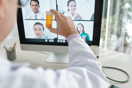 Close-up of doctor showing bottle of medicine to his colleagues on computer monitor during online...