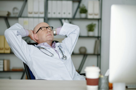 Mature doctor in white coat sitting at his workplace and relaxing after hard work at hospital