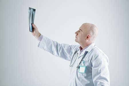 Mature doctor in white coat examining the x-ray image in his hand standing against the white backgroundの写真素材