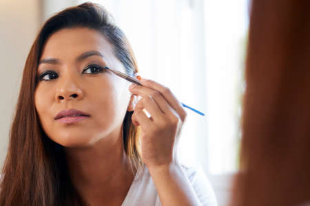 Concentrated young woman applying eye shadows with thin make-up brushの写真素材