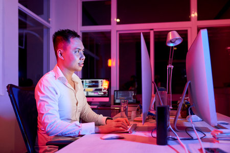 Positive software developer working on computer at office table, pink neon lightの写真素材