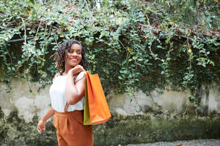 African happy woman holding shopping bags while walking through the street outdoors
