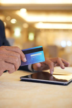 Hands of senior businessman using credit card to pay for purchases he makes online via application on tablet computerの写真素材