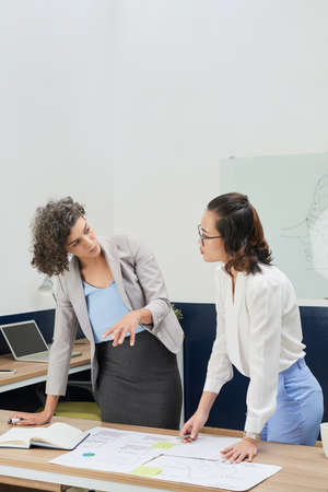 Serious young female entrepreneur discussing statistics document with her colleague at meetingの写真素材
