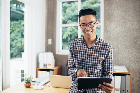Young entrepreneur working on tablet computer in his home office, he is answering e-mails and...