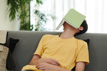 Teenage boy fell asleep on sofa in living room with opened book on his face