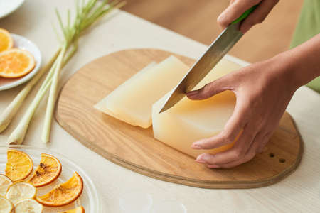 Hands of woman cutting soap base with sharp knife when making cleansing bars at homeの写真素材