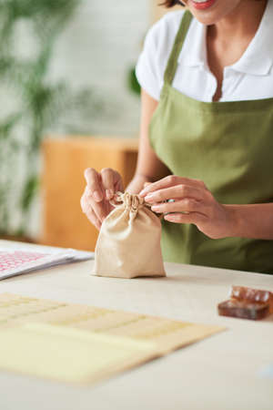 Positive creative woman tying cotton bag with soap she made for selling onlineの写真素材