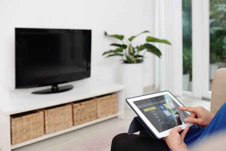 Hands of elderly woman using smart home app on digital table when changing temparature in living...