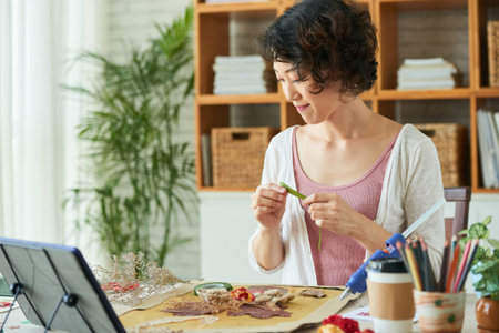 Young woman using floral paper tape to attach dried flowers, petals, leaves to canvasの写真素材